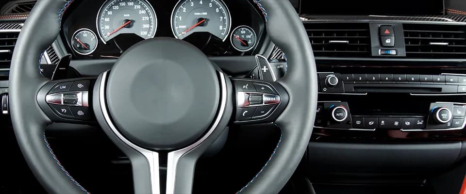 Kennzahlen sind erst in ihrer Gesamtheit aussagekräftig bzw. müssen so betrachtet werden. Nahaufnahme des Lenkrads und Armaturenbretts eines modernen Luxusautos. Das Lenkrad verfügt über verschiedene Bedienelemente, darunter Tasten für Telefon, Lautstärkeregelung und Tempomat. Im Hintergrund sind die Geschwindigkeitsanzeige, Drehzahlmesser und Lüftungsschlitze zu sehen. Die Mittelkonsole enthält Klimasteuerungen und ein Infotainmentsystem. Das Interieur ist mit eleganten Materialien wie glänzendem Kunststoff und roten Lederakzenten ausgestattet.